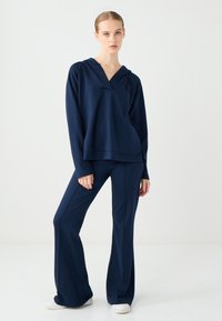 Marineblaues Sweatshirt mit V-Ausschnitt und Kapuze, kombiniert mit passenden weit geschnittenen Hosen. Glatte Textur, lässiges Design und keine sichtbaren Muster.