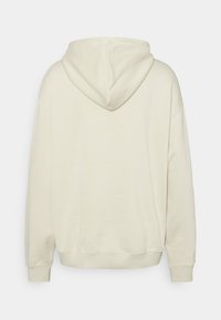 Felpa beige chiaro con una texture morbida, caratterizzata da un ampio cappuccio, maniche lunghe e una vestibilità comoda. Tessuto liscio senza motivi visibili.