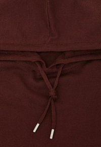 Burgundská mikina s žebrovanou texturou, vybavená stahovacím šňůrkou u krku a stříbrnými zakončeními. Hladká látka s přiléhavým střihem.