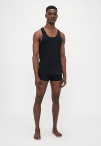 Schwarzes Tanktop und Boxershorts aus glattem Stoff. Das Tanktop hat breite Träger und eine lockere Passform. Die Boxershorts verfügen über einen elastischen Bund.