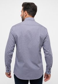 Camicia a scacchi in navy e bianco con maniche lunghe, polsini a bottone e colletto a punta. Il materiale sembra liscio e leggero.