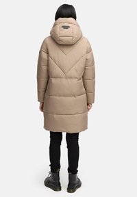 Beige, polstret frakke med hætte, der har et chevron-quiltet design, lange ærmer og en mid-length pasform. Bæres med sorte bukser og støvler.