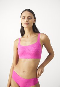 Ružový pulóverový bralet a zodpovedajúce hipster spodné prádlo, s textúrovaným vzorom, výrezmi so zubatými okrajmi a hladkým, elastickým materiálom.