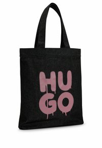 Sac fourre-tout noir avec de larges anses et un grand texte rose style graffiti "HUGO" sur le devant.