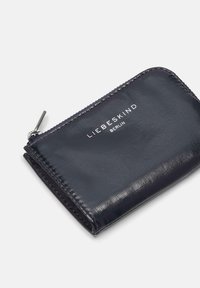 Granatowy skórzany portfel o gładkiej fakturze, z srebrnym zamkiem błyskawicznym i białym wytłoczonym logo "LIEBESKIND BERLIN" na przodzie.