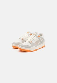 Zapatos deportivos con una parte superior de cuero blanco y gris con acentos en naranja, un collar acolchado y una suela texturizada para mayor tracción.