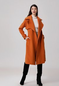 Manteau en mélange de laine orange avec un col cranté, des manches longues et des poches latérales. Le manteau a une coupe décontractée et une longueur en dessous du genou.
