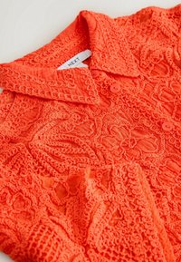 Chemise boutonnée orange vif avec broderie en dentelle florale complexe et col pointu, étiquetée avec l’étiquette de marque "NEXT".