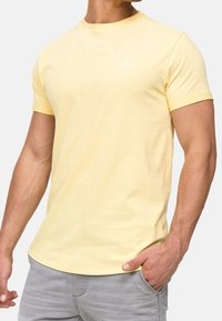 Yellow cotton t-shirt with short sleeves, round neckline, and a small logo on the chest. Smooth texture and casual fit.