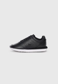 Sneaker in pelle nera con lacci neri, suola bianca e logo "cK" in rilievo sul lato, mostrato di profilo su sfondo bianco.