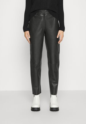 Pantalons en cuir noir à coupe droite, avec des panneaux élégants et une texture lisse. Associés à des bottines blanches à la cheville.
