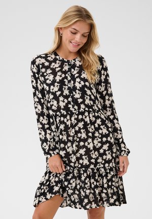 Abito nero floreale con maniche lunghe, orlo arricciato e dettagli con bottoni. Presenta un motivo floreale bianco su un tessuto leggero.