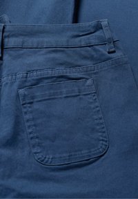 Sötétkék anyag sima textúrával, hátsó zsebbel és övtartókkal. A varrás látható az éleken és a zsebnél.