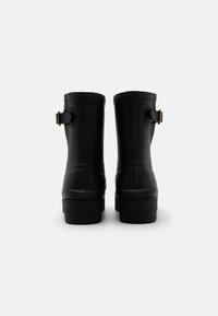 Black rubber boots with a rounded toe, mid-calf height, textured surface, and a gold buckle accent on the side.