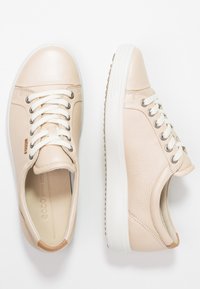 Beige leather sneakers with white rubber soles, lace-up design, silver eyelets, and a textured finish on the upper.