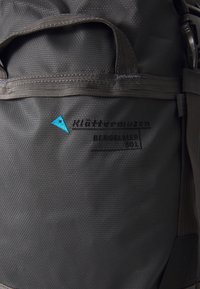 Zaino in tessuto nero con superficie testurizzata, caratterizzato da un logo blu e dal nome del modello. Include maniglie superiori e spallacci resistenti.
