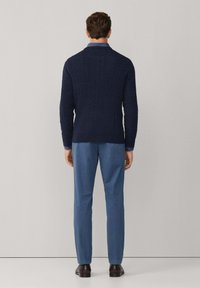 Marineblauwe kabelgebreide trui met hoge kraag, gecombineerd met lichtblauwe broeken. Donkerbruine schoenen maken de outfit compleet. Eenvoudig, gestructureerd ontwerp.