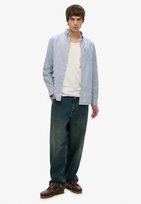 Gestreept blauw shirt met knopen, witte tanktop, losvallende blauwe spijkerbroek en donkerbruine veterschoenen.