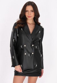 Schwarze Kunstlederblazer mit Perlenverzierungen, doppelt geknöpftem Design, scharfen Revers und Seitentaschen, kombiniert mit einem passenden Minirock.