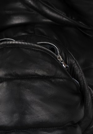 Veste en cuir noir avec texture matelassée. Équipée d'une poche zippée métallique avec des accessoires en argent, surface lisse et éclat discret.