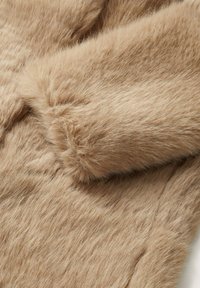 Gros plan sur un tissu en fausse fourrure beige montrant une texture douce et dense avec une section pliée mettant en valeur son moelleux et sa chaleur.
