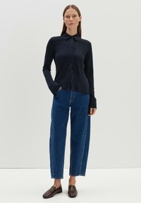 Navy long-sleeve button-up shirt paired with high-waisted blue denim jeans. Shoes are dark brown slip-ons, with straight-leg jeans featuring side seams.