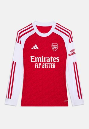 Červený futbalový dres s dlhým rukávom a bielymi akcentmi. Medzi prvky patrí vyšívané logo, text "Emirates Fly Better" a charakteristické pruhované rukávy.