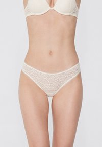Culotte en dentelle de couleur crème présentant des motifs floraux, une texture douce et des bords festonnés. Conçue avec une taille basse pour plus de confort.