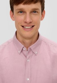 Hellrosa Hemd mit Knopfleiste und Kragen, das eine subtile Struktur und kontrastierende weiße Knöpfe aufweist. Einfaches Design, ohne Muster oder Akzente.