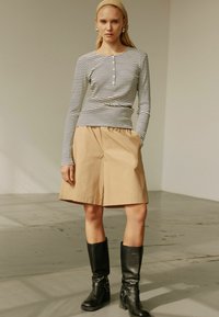 Maglietta a maniche lunghe a righe grigia e bianca, abbinata a pantaloni corti beige fino al ginocchio e stivali neri alti fino al ginocchio con fibbie. Tessuto liscio.