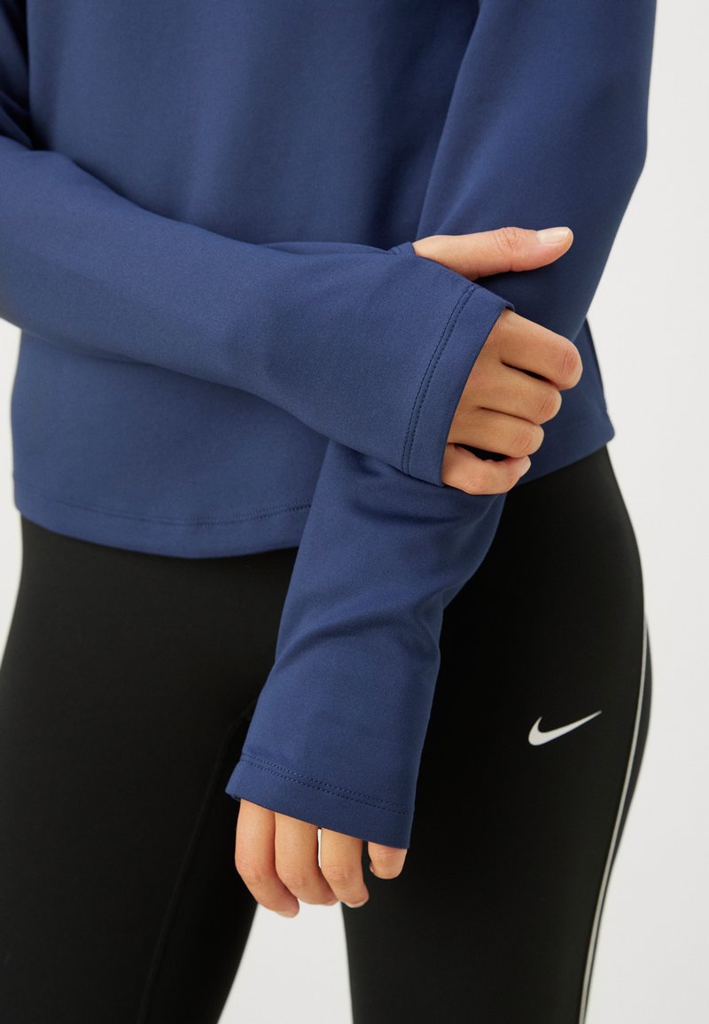 Marineblå langærmet træningstrøje med tommelfingerhuller, glat tekstur og rundede kant, parret med sorte leggings med en hvid logoaccents.