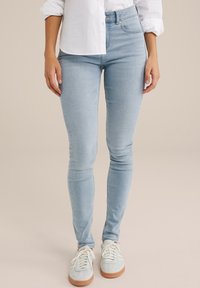 Helle blaue Skinny-Jeans aus Denim, mit hoch geschnittenem Bund und dezenten Ausbleichungen, kombiniert mit lässigen weißen Sneakern.