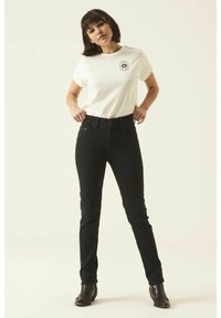 Camiseta de algodón blanca con un logo negro en el pecho, combinada con jeans negros de cintura alta. Modelo lleva botas negras hasta el tobillo.
