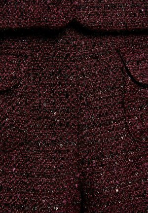 Tessuto marrone scuro con piccole paillettes, caratterizzato da un design strutturato e tasche visibili, creando un aspetto a strati.