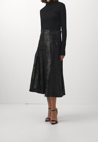 Svart polokrage topp kombinerad med en hel längd svart paljettkjol, som har en mjuk textur och glänsande yta. Svarta klackar med ankelrem.