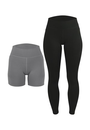 Frau steht barfuß und trägt ein graues Neckholder-Crop-Top mit weißer Umrandung und passende hoch taillierte Biker-Shorts vor einfarbigem Hintergrund.