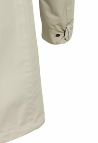 Manche de manteau beige avec un poignet boutonné et des coutures visibles verticales et horizontales sur un tissu lisse.