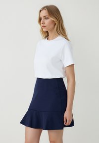 Witte korte mouwen t-shirt gecombineerd met een knielange marineblauwe uitlopende rok. Gladde stof met een getailleerde taille en een gerimpelde zoom.
