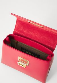 Sac à main en cuir rose rectangulaire avec un fermoir doré, doté d'une doublure intérieure douce et d'une poche zippée, affichant le logo de la marque à l'intérieur.