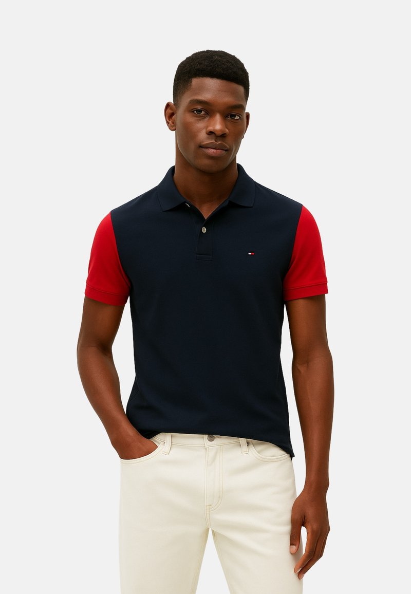 Polo de color azul marino con mangas rojas, mezcla de algodón, con tapeta de dos botones, detalle sutil del logo en el pecho, combinado con vaqueros de color claro.