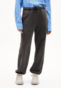 Grijze, losse sweatpants met een elastische tailleband en een verstelbaar trekkoord, gecombineerd met een blauw gestreept overhemd met knopen en witte sneakers.