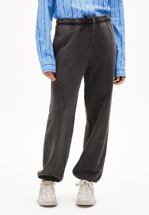 Graue, locker sitzende Sweatpants mit elastischem Bund und verstellbarem Kordelzug, kombiniert mit einem blauen gestreiften Hemd mit Knöpfen und weißen Turnschuhen.