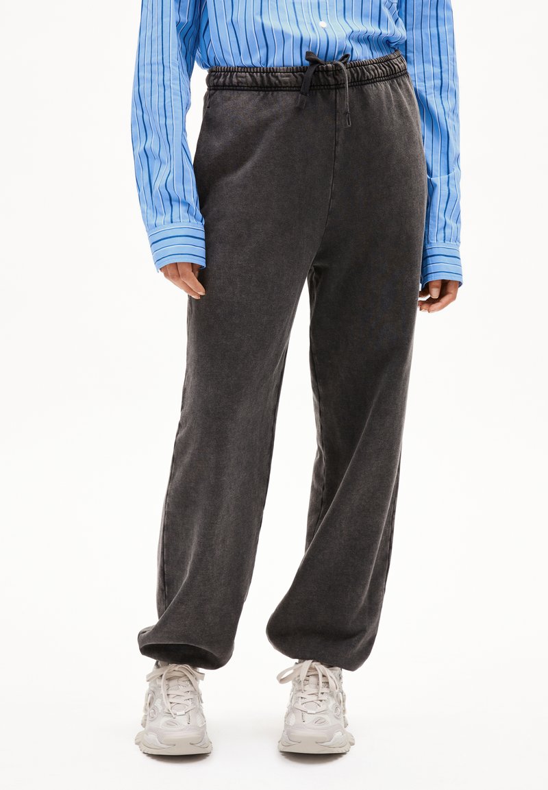 Grijze, losse sweatpants met een elastische tailleband en een verstelbaar trekkoord, gecombineerd met een blauw gestreept overhemd met knopen en witte sneakers.