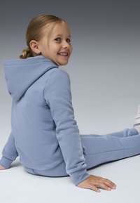 Hoodie azul claro e calças de treino a condizer, feitas de tecido suave, com um bolso tipo canguru e punhos canelados, repousando sobre uma superfície lisa.