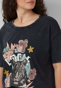 Zwarte graphic T-shirt met een tijgerillustratie en kleurrijke bloemaccenten. Ronde halslijn, korte mouwen en een relaxed fit.