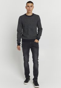 Mørkeblå sweater med et struktureret mønster, parret med mørke jeans og sorte sneakers. Sweateren har en rund halsudskæring og ribbestrikkede manchetter.