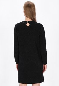 Vestido negro de punto con mangas largas, acabado texturizado y un detalle de ojal en la espalda. Presenta una silueta sencilla y recta.