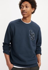 Navy sweatshirt in katoenmix, ronde hals, geborduurd logo op de borst, geribde manchetten en zoom, zachte textuur, relaxed fit.
