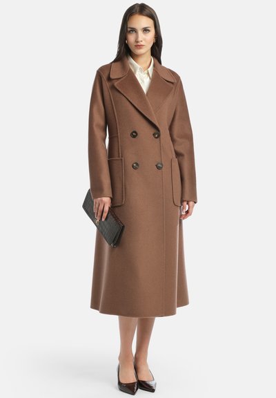 Bruin dubbelzijdig wollen coat met een gekarteld kraag, zijzakken en een middellange snit. Het model draagt een zwarte gestructureerde clutch en punkteerhakken.