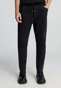 Czarne dresowe spodnie z mieszanki bawełny, z elastycznym pasem, sznurkiem i bocznymi kieszeniami, zwężanym krojem nogawki oraz subtelną teksturą.